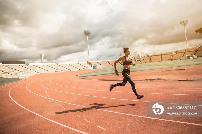 Young woman running during sunny evening on stadium track