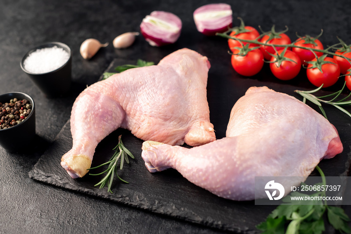 two raw chicken legs with spices and herbs on a stone background