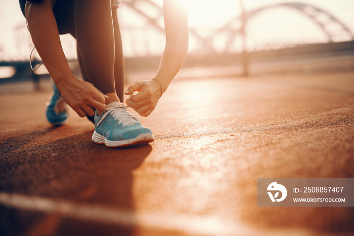 Close up of sporty caucasian woman kneeling and tying shoelace on court in the morning. Sometimes th