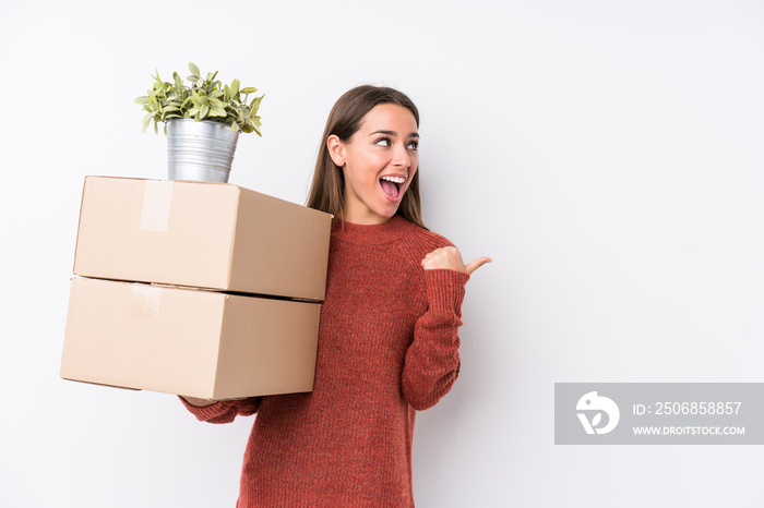 Young caucasic woman holding boxes isolated points with thumb finger away, laughing and carefree.