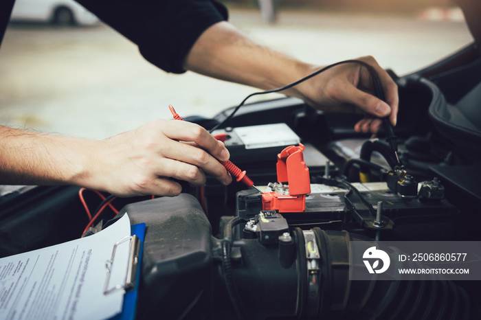 Car mechanic is using the car battery meter to measure various values and analyze it.