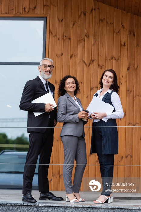 interracial business partners and real estate broker smiling near building outdoors