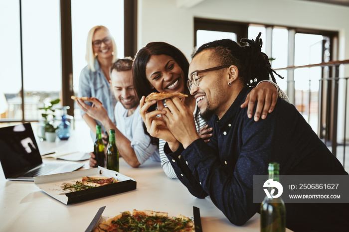 Office colleagues laughing over pizza and beers after work