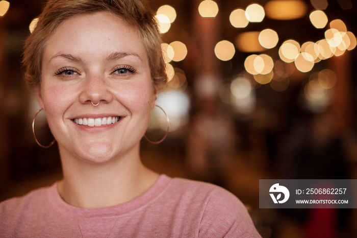 Close-up portrait of happy businesswoman sitting against illuminated lights in cafe