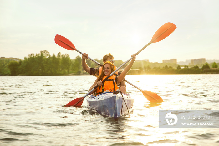 快乐的年轻高加索夫妇在河上划皮划艇，背景是日落。休闲娱乐