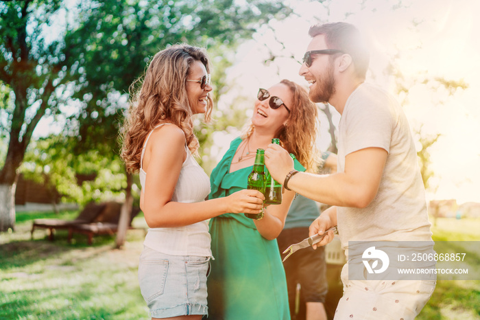 Group of friends having beers and cooking on garden barbecue. Lifestyle, leisure concept