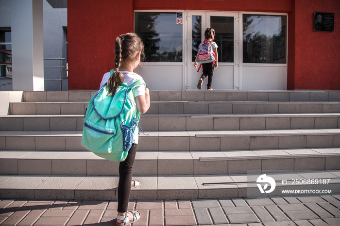 Back to school education concept with girl kids, elementary students, carrying backpacks going to cl