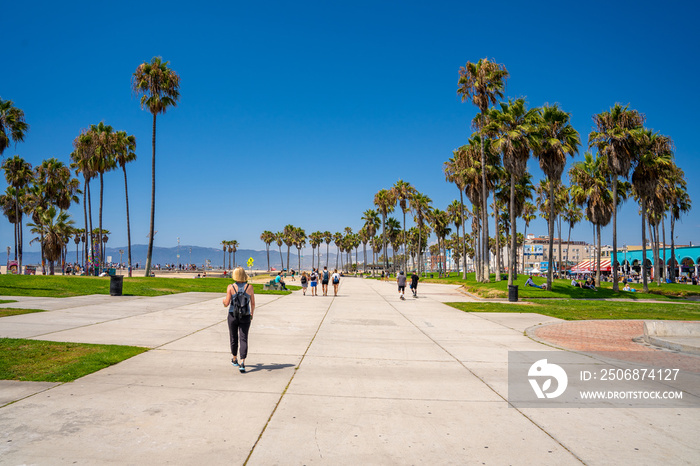 Sunny spirit in California at the Venice beach district. People walking or driving bicycles down the