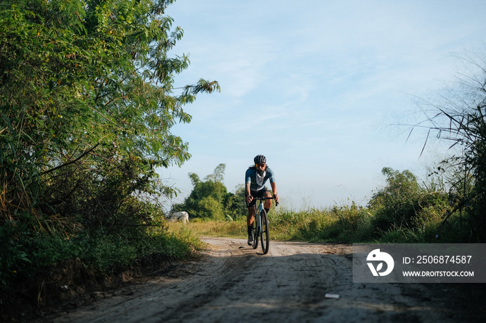 A young bearded cyclist is biking through a dirt path.