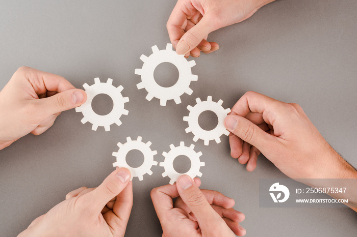 cropped view of people holding white gears on grey background