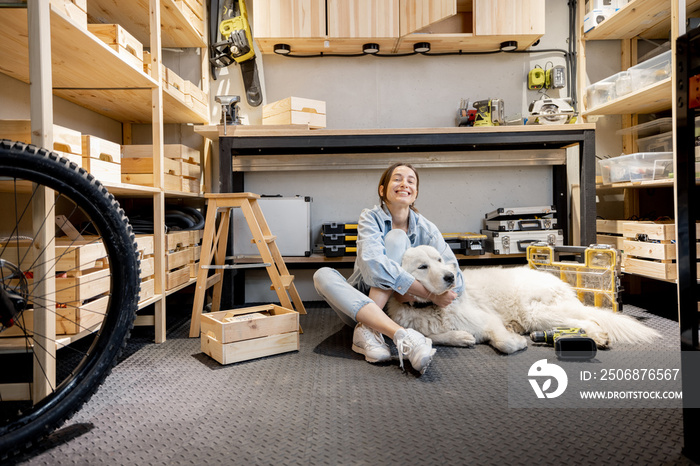 Portrait of a young handywoman sitting with her huge white dog in the home workshop. DIY concept