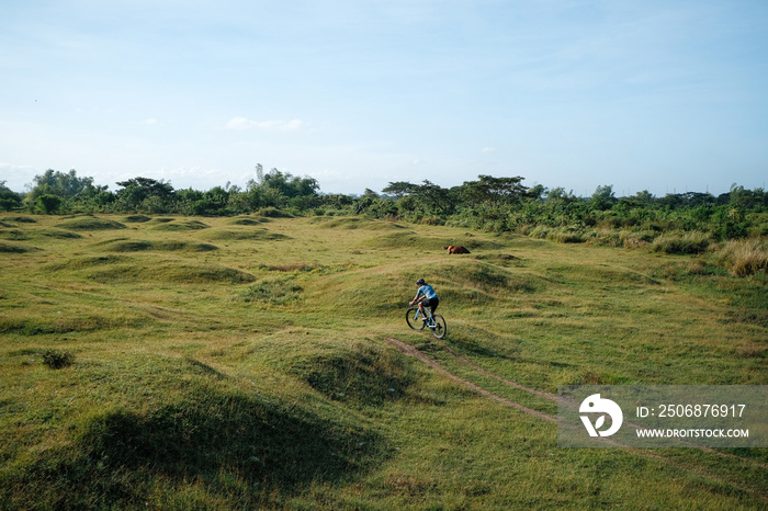 A young bearded cyclist is biking through a field