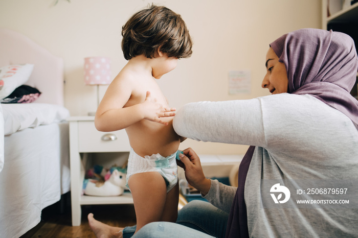 Mother changing diaper of son in bedroom at home