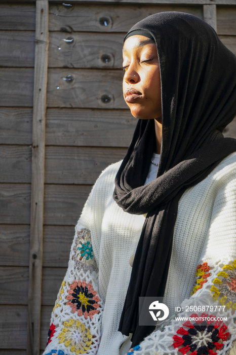 Portrait of woman wearing hijab with eyes closed sitting outdoors