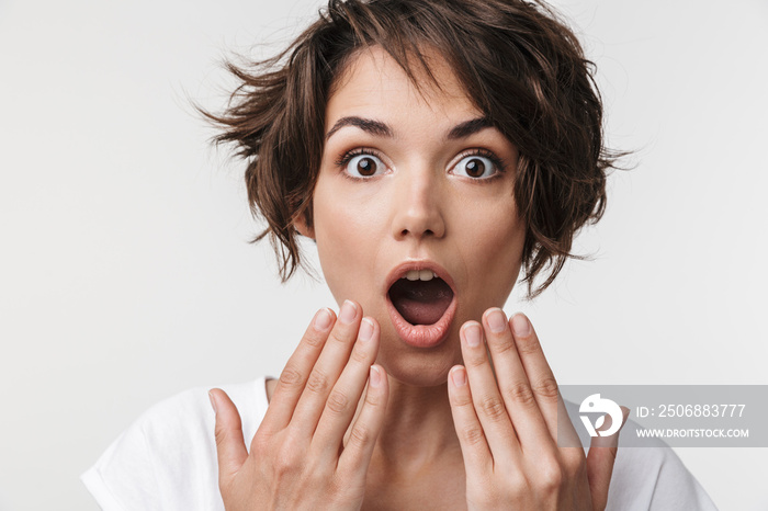 Portrait of excited woman with short brown hair in basic t-shirt covering her mouth with hands