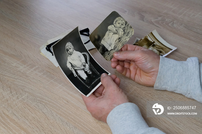 old male hands hold retro family photos over an album with vintage monochrome photographs in sepia c