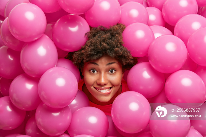 节日期间，一位迷人的卷发女士在粉色气球中摆姿势，很高兴收到祝贺