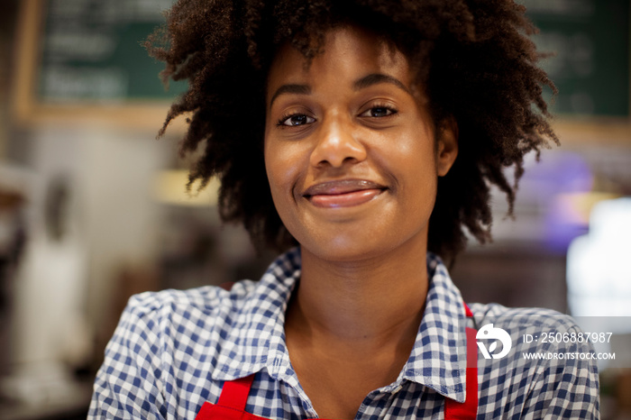 Close-up portrait of smiling female barista with curly hair standing in cafe