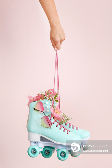 Woman holding vintage roller skates with flowers and sunglasses on light background