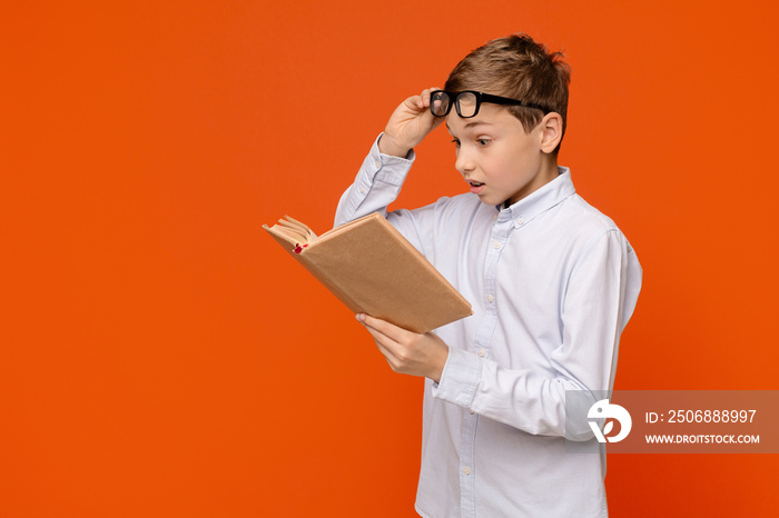 Emotional teenager reading exciting book, raising his glasses