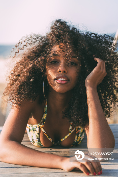 美丽的年轻黑人女子躺在海滩的一座木制步行桥上。