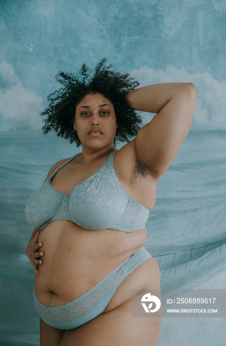 portrait of a plus size afro indigneous person standing with hand on tummy and hand in hair