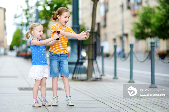 Two cute little sisters playing outdoor mobile game on their smart phones