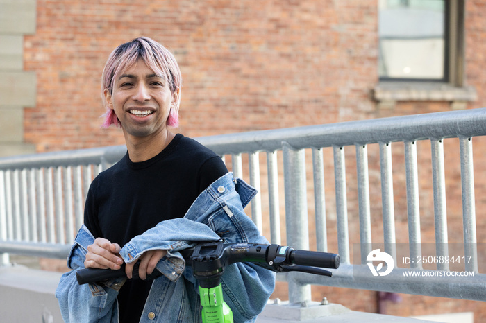 Non-binary person outside with an electric scooter.