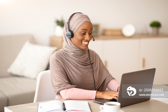 戴着头巾、戴着耳机的非裔美国女商人在hom使用笔记本电脑进行在线交流