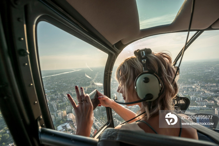 Beautiful blonde women taking photo of cityscape with smart phone in helicopter.