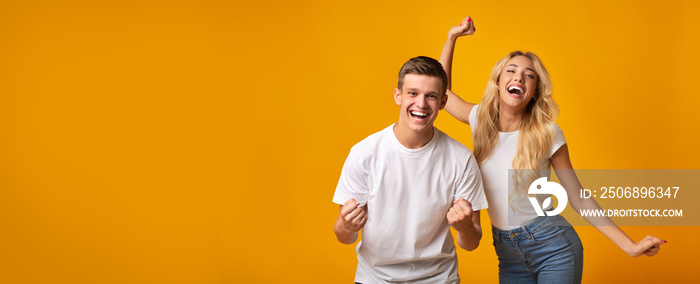 Excited millennial couple rejoicing success over yellow background