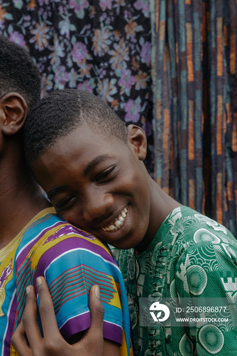 African boy in ankara resting on brothers shoulder while smiling