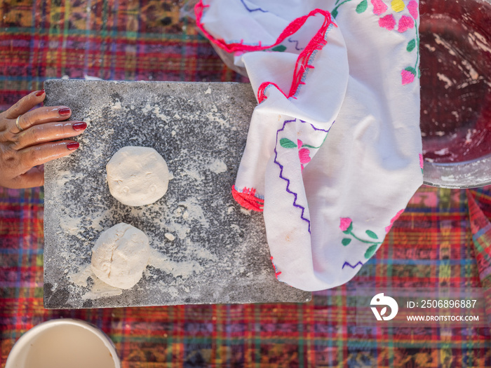 Overhead image of a hand on a metate with masa for tortillas