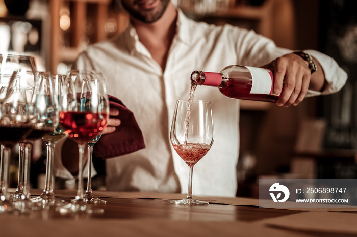 Professional young bartender pouring down pink champagne