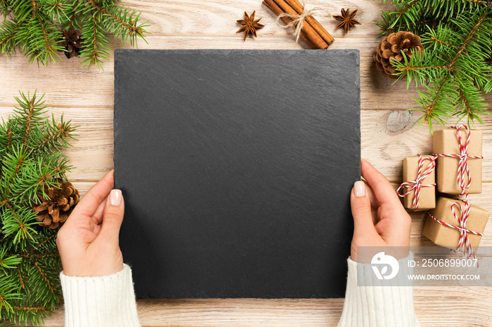 Famale hand hold slate platter on brown background with christmas decoration. slate board isolated. 