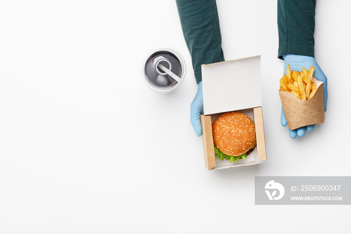 Order in fast food restaurant. Waiter in rubber gloves gives burger in cardboard box, and french fri