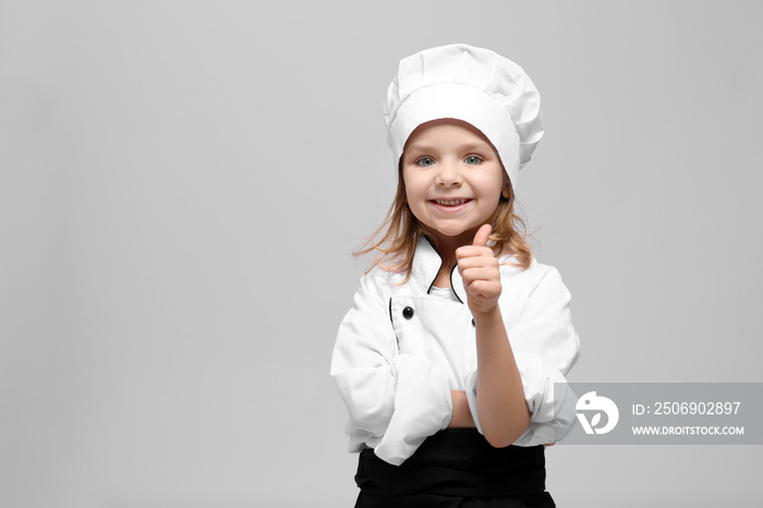 Cute girl in chef uniform on light background