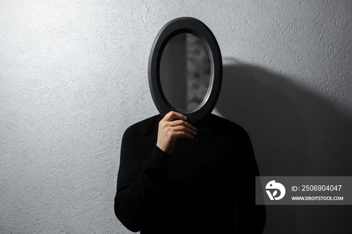 Dramatic portrait of man with black mirror on face. Background of white textured wall.