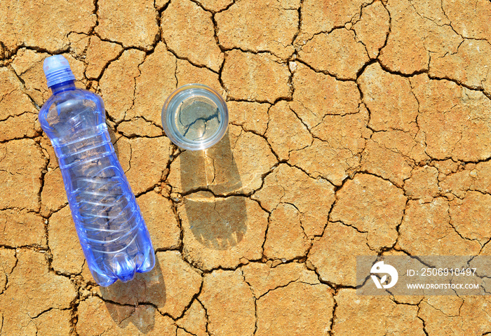 一瓶又一杯的水放在干裂的土壤上。全球变暖的概念。