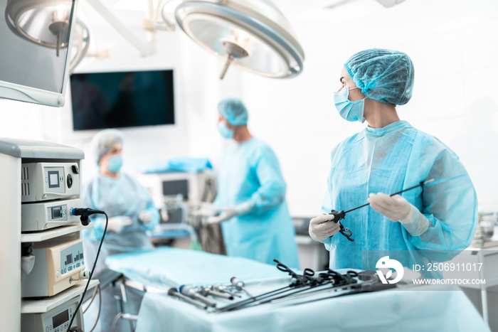身穿蓝色无菌长袍的女医务工作者站在手术台附近的腰部肖像
