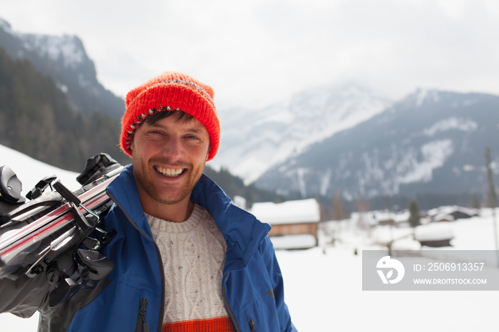 Portrait smiling young man carrying skis in snow