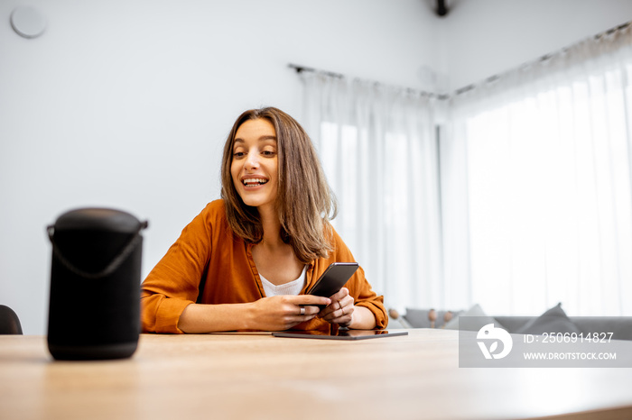 Young cheerful woman controlling home devices with a voice commands, talking to a smart column at ho