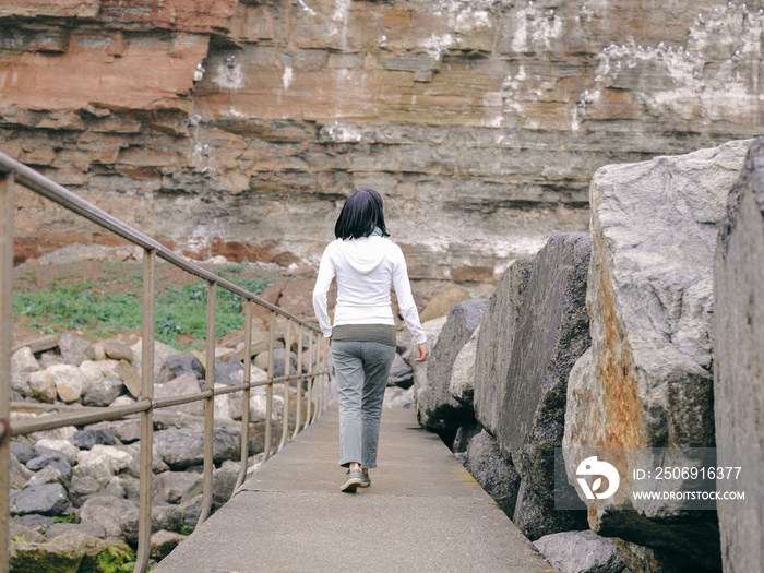 英国，一名女子在岩石景观中走在人行道上的后视图
