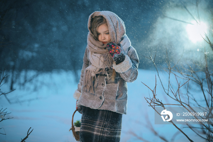 little child girl with a basket goes and looks for the first flowers under the snow in the forest in