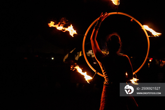 fire-eater, fire dancer with flaming hoop in night show at medieval festival with black background