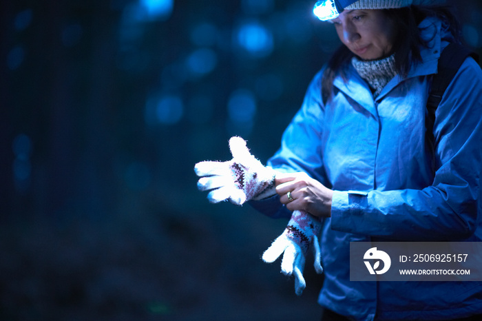 女徒步旅行者戴着手电筒在森林里戴手套