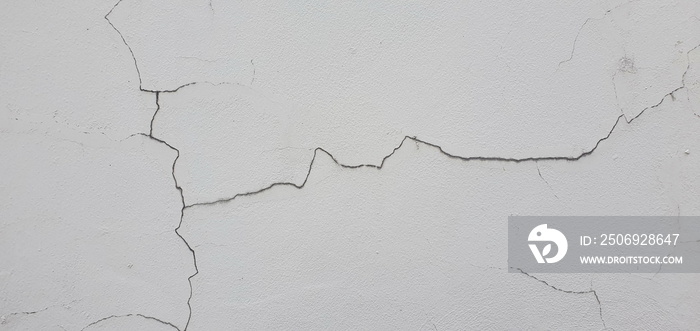 The white painted cement wall, cracks are visible until a long fissure is visible and rainwater can 