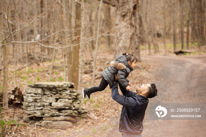 Side view of happy father picking up daughter while standing on road against bare trees in forest