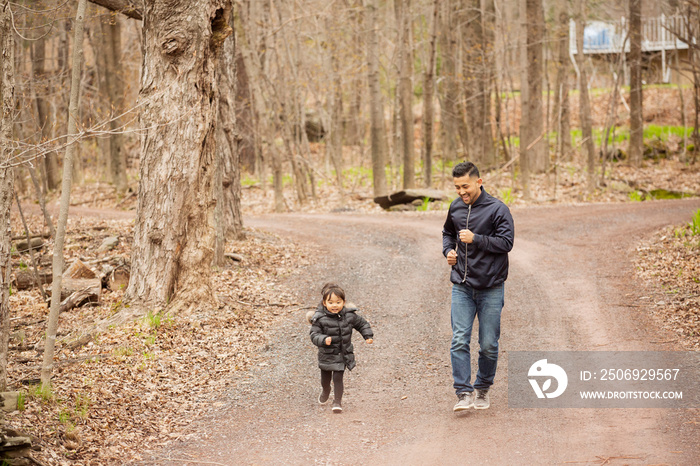 Happy father running with playful daughter on road against bare trees in forest