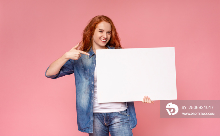 Red-haired girl holding blank advertising board and pointing on it